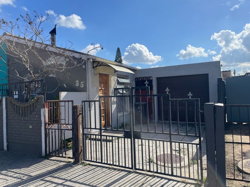 Front elevation of a residential property featuring a paved driveway, single garage, and metal security gate entrance.