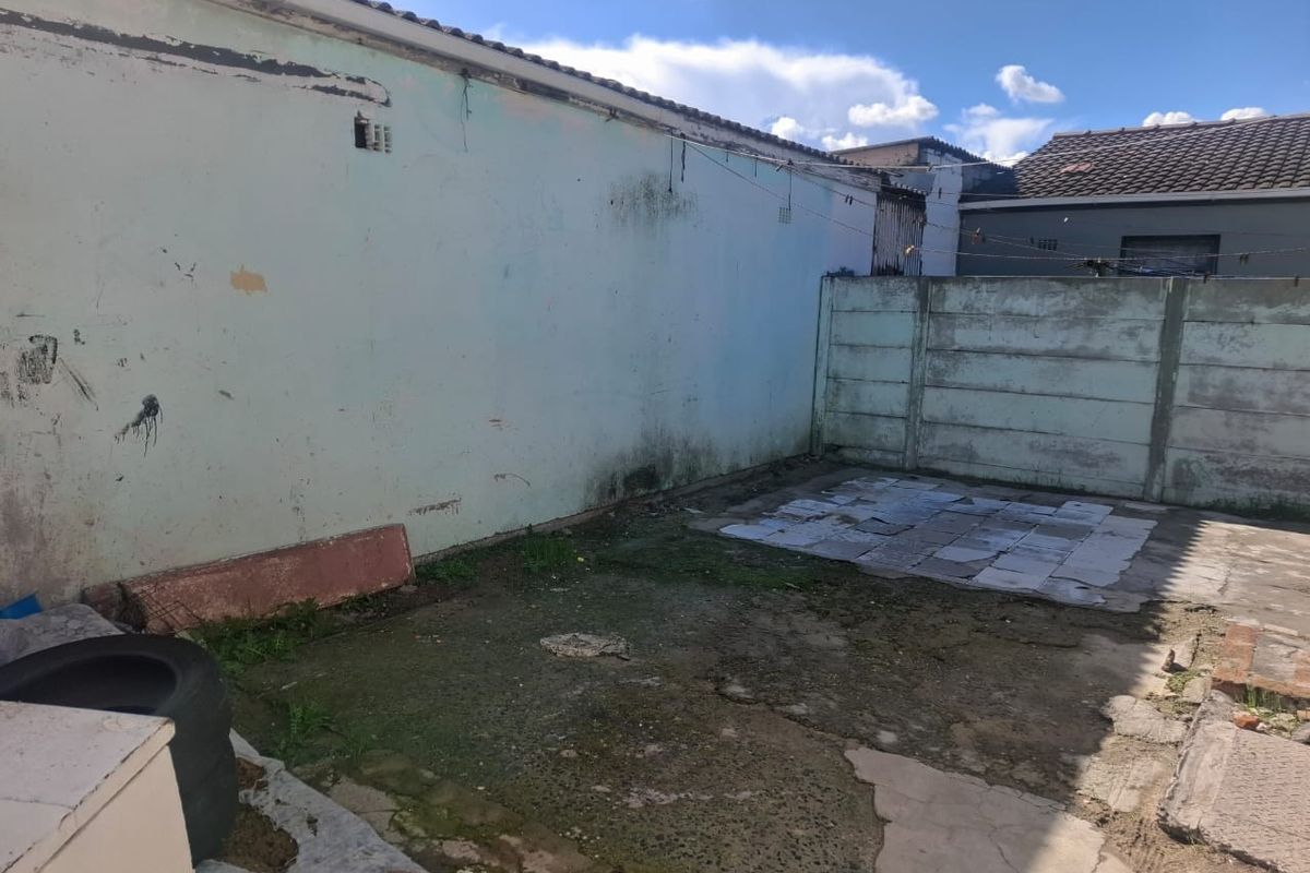 A rear outdoor area featuring a concrete boundary wall and paved section, requiring maintenance and landscaping to improve its overall condition and appeal.