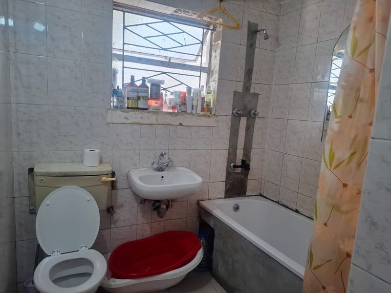A functional bathroom featuring a bathtub, wall-mounted basin, and toilet, with tiled walls and security bars on the window.