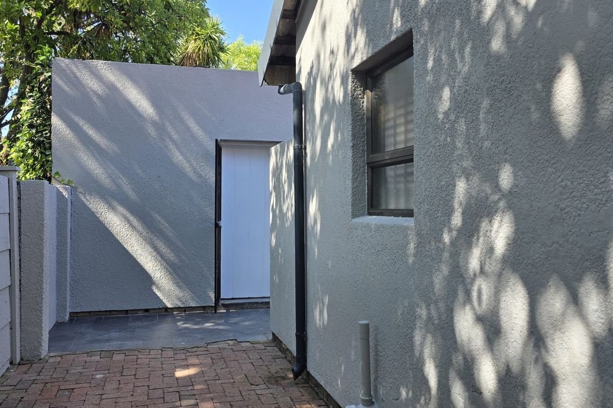 A view of the rear exterior area featuring a paved walkway, textured walls, and a functional side entrance.