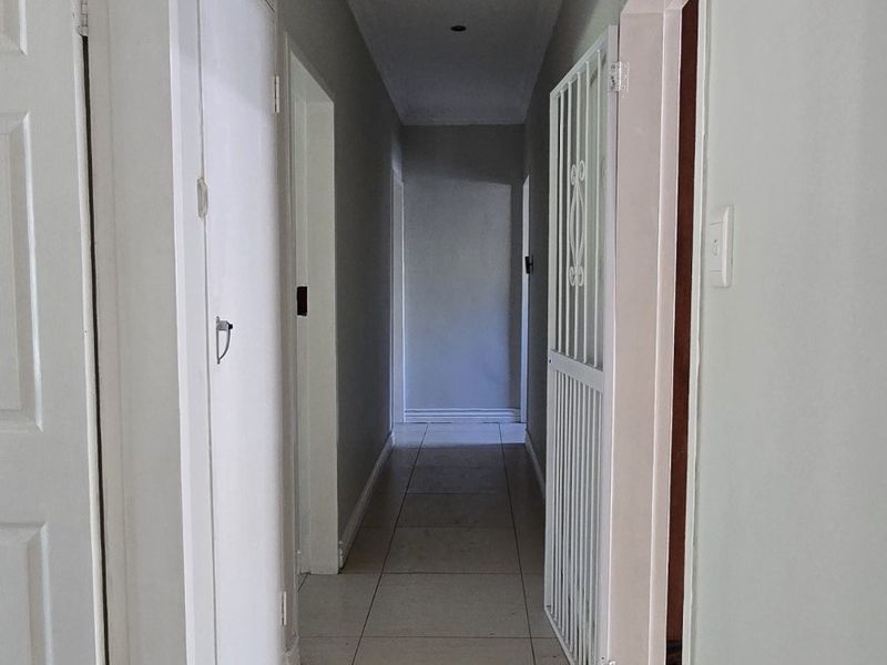A clean, neutral hallway featuring tiled flooring, recessed downlighting, and built-in storage cupboards, providing access to multiple rooms.
