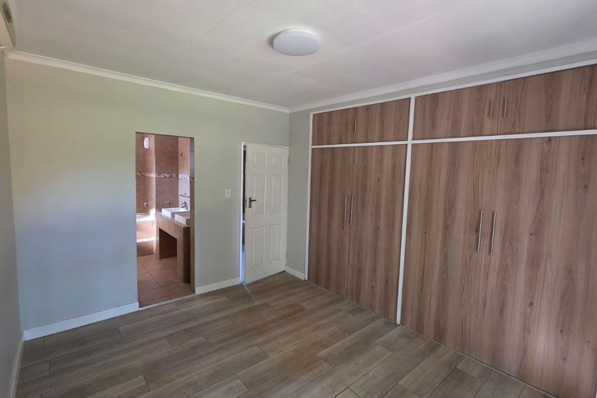 Spacious bedroom featuring wood-look tiled flooring, extensive built-in cupboards, an air conditioning unit, and direct access to an en-suite bathroom.