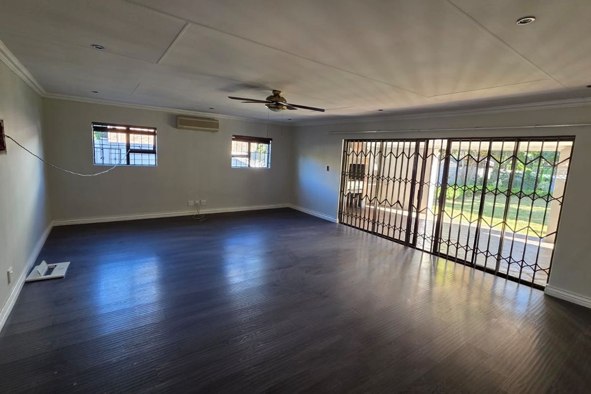 Spacious, empty living area featuring dark laminate flooring, recessed lighting, a ceiling fan, air conditioning, and large sliding doors with security gates leading outdoors.