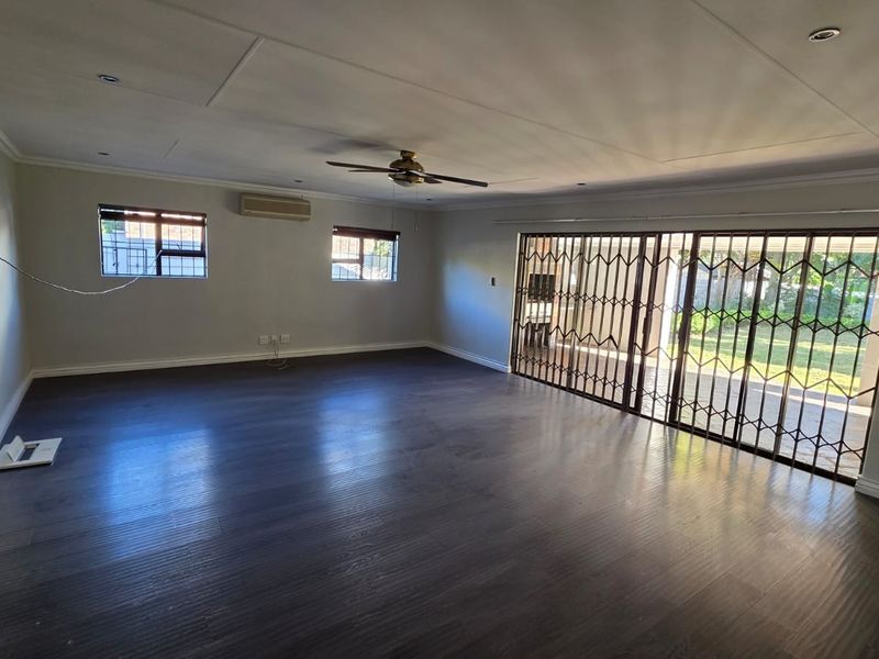 Spacious, empty living area featuring dark laminate flooring, recessed lighting, a ceiling fan, air conditioning, and large sliding doors with security gates leading outdoors.