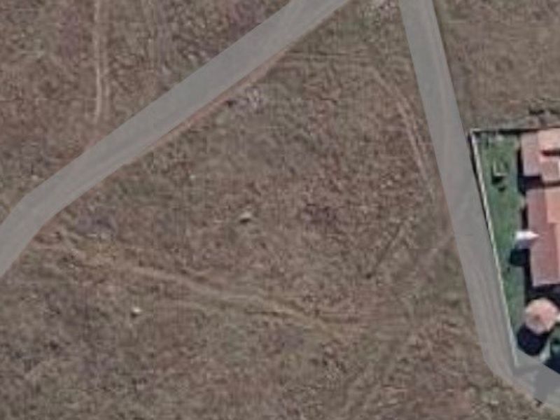 An aerial view of a vacant residential plot showing surrounding road infrastructure and neighboring properties.
