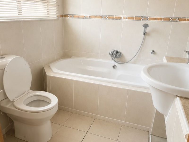 A functional bathroom featuring a built-in bathtub, pedestal washbasin, toilet, and neutral ceramic tiling throughout.