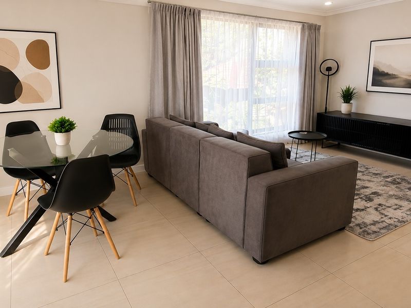 A bright and modern open-plan living and dining area featuring neutral tiled flooring, recessed lighting, and large sliding glass doors with curtain treatments.
