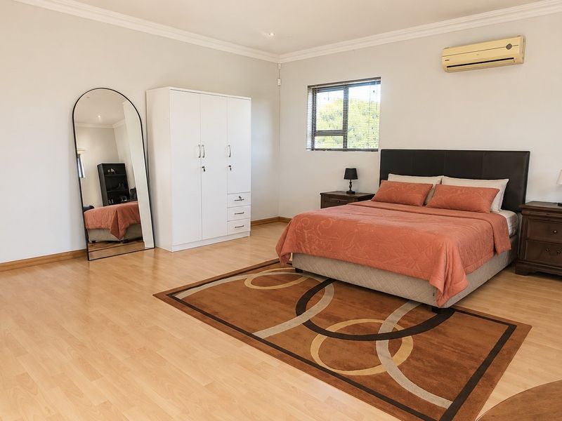 Spacious bedroom featuring light laminate flooring, a wall-mounted air conditioning unit, and neutral wall finishes.