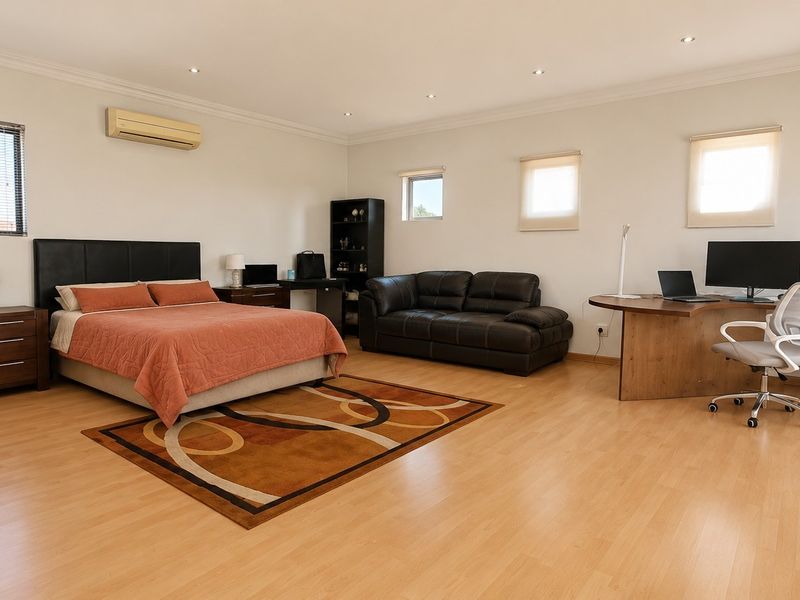 Spacious bedroom featuring laminate flooring, recessed downlighting, and a wall-mounted split-system air conditioner, offering a versatile layout with ample natural light.