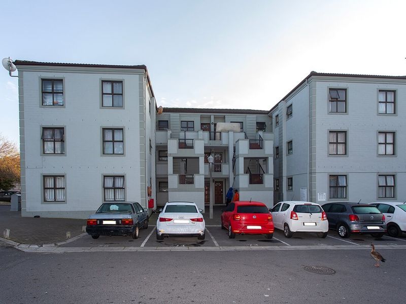 Front elevation of a multi-story apartment complex featuring a paved parking area and external access balconies.
