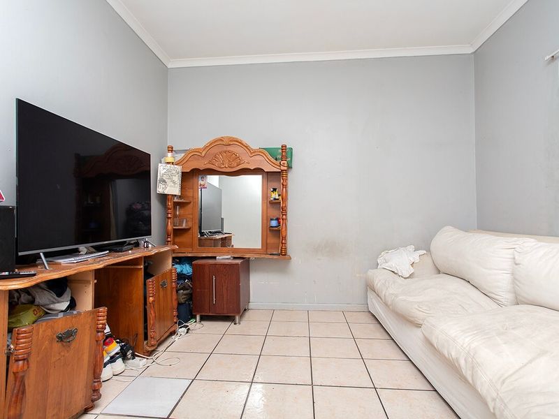 A living room featuring tiled flooring and coved ceilings, currently showing signs of wear on the wall surfaces.