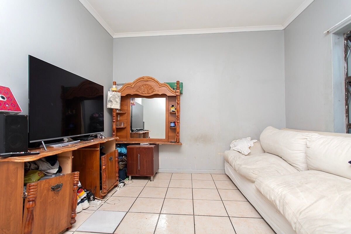 A living room featuring tiled flooring and coved ceilings, currently showing signs of wear on the wall surfaces.