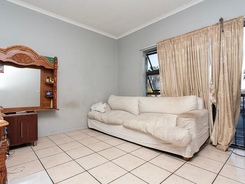 A living room featuring tiled flooring and a sliding door leading to a balcony, with walls showing signs of wear and staining.