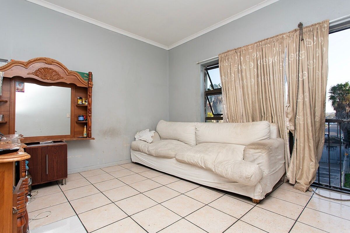 A living room featuring tiled flooring and a sliding door leading to a balcony, with walls showing signs of wear and staining.