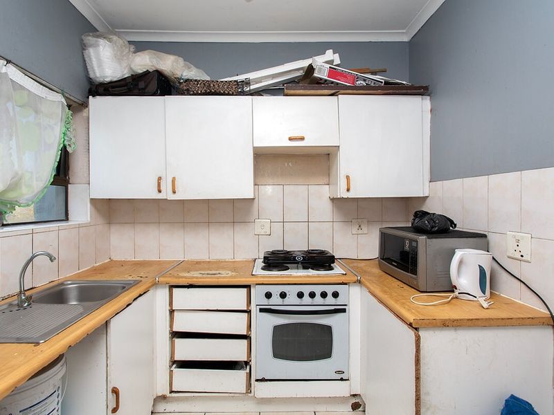 A compact kitchen featuring white cabinetry, a stainless steel sink, and a built-in oven, currently showing signs of wear and requiring cosmetic updates.