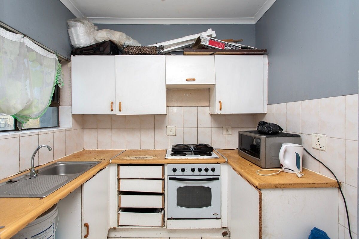 A compact kitchen featuring white cabinetry, a stainless steel sink, and a built-in oven, currently showing signs of wear and requiring cosmetic updates.
