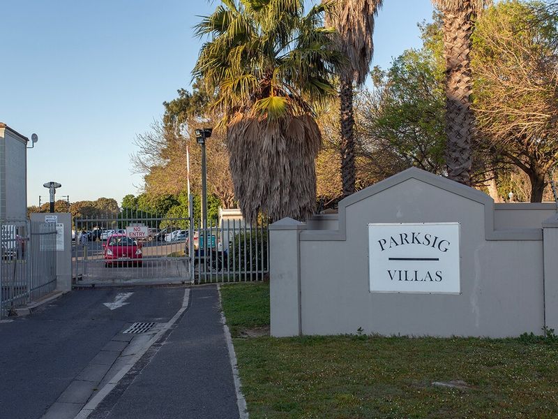 Entrance view of the Parksig Villas apartment complex, featuring a secure gated access point, paved driveway, and established landscaping.