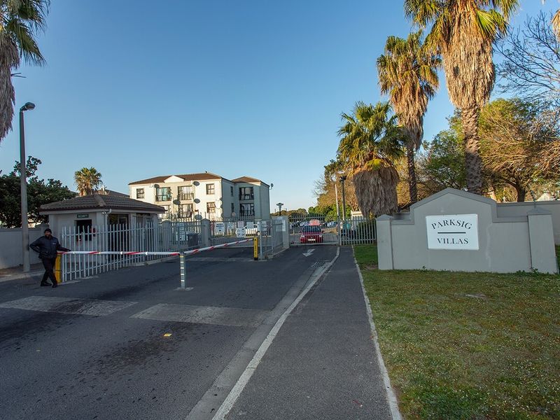 The entrance to Parksig Villas featuring a secure gated access point, guard house, and paved driveway leading into the apartment complex.