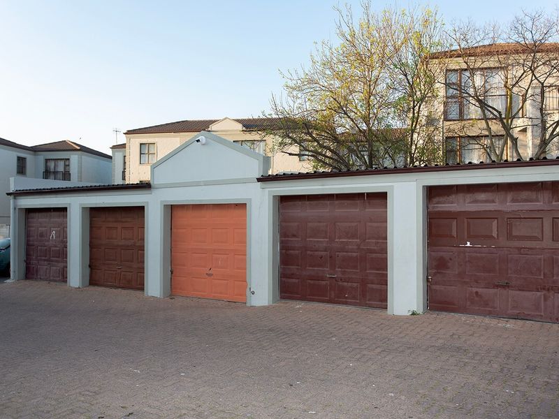 A row of multiple garage units with paved driveway access, featuring standard sectional doors and exterior security lighting.