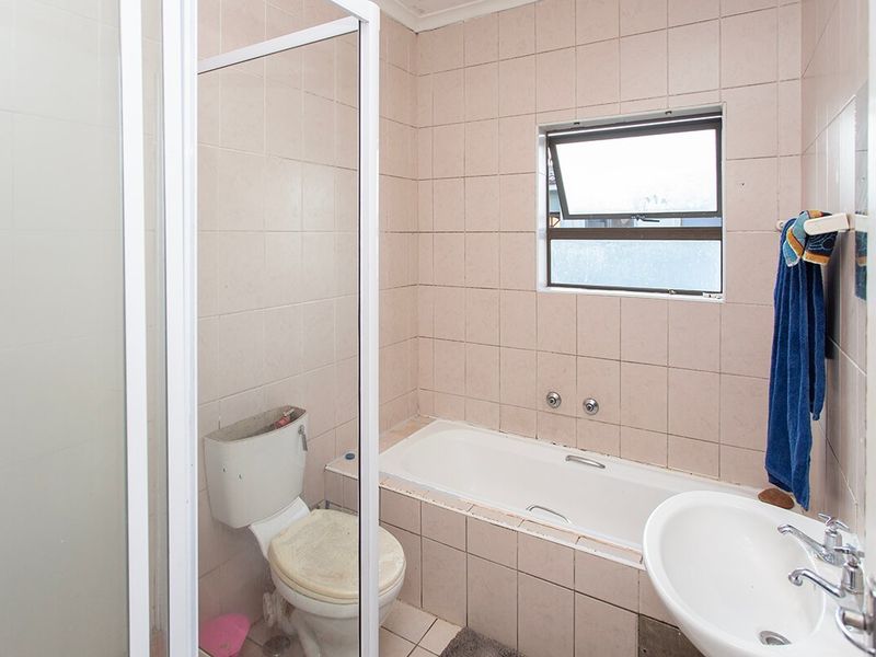 A dated bathroom featuring a bathtub, shower enclosure, pedestal basin, and toilet, finished with neutral wall and floor tiles.