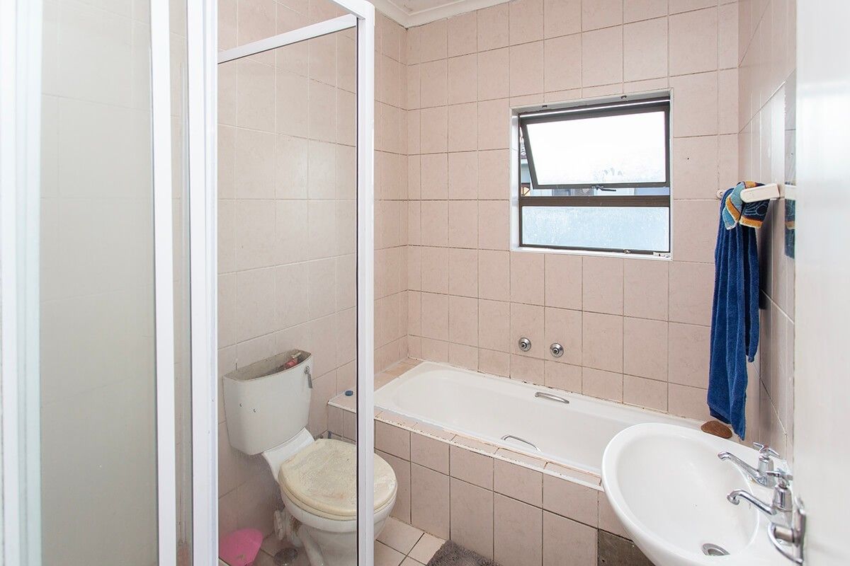 A dated bathroom featuring a bathtub, shower enclosure, pedestal basin, and toilet, finished with neutral wall and floor tiles.