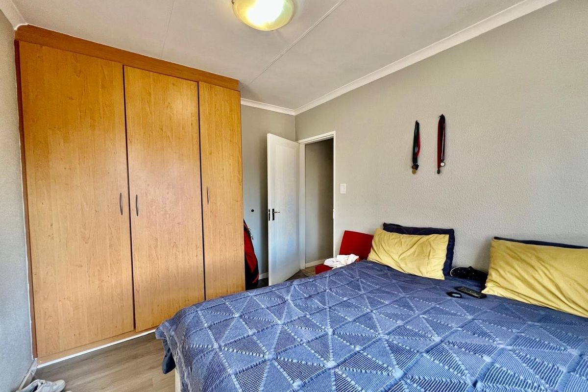 A functional bedroom featuring built-in wooden wardrobes, laminate flooring, and a neutral color palette, offering a practical and comfortable living space.
