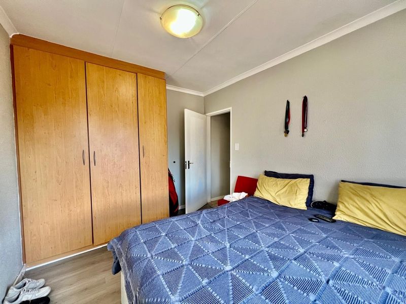 A functional bedroom featuring built-in wooden wardrobes, laminate flooring, and a neutral color palette, offering a practical and comfortable living space.