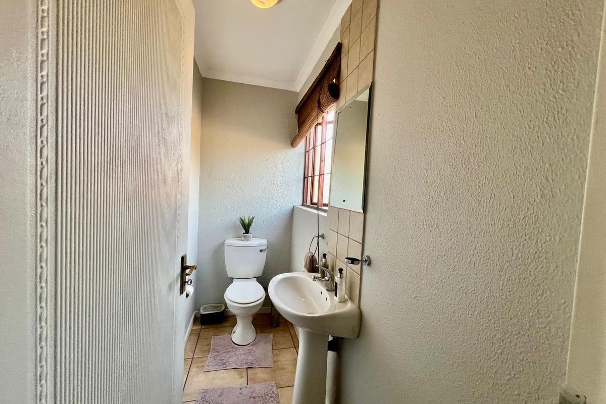 A compact guest bathroom featuring a pedestal basin, toilet, tiled flooring, and a tiled splashback area.