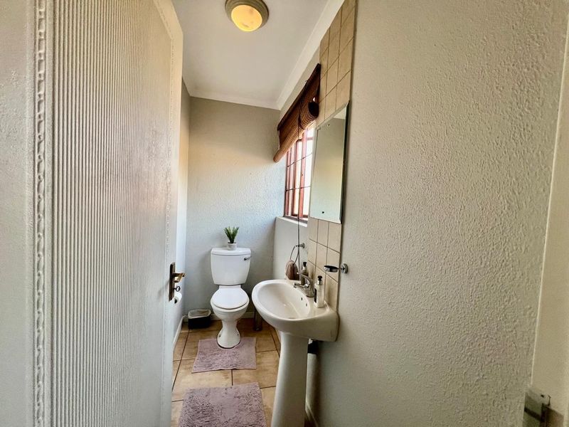 A compact guest bathroom featuring a pedestal basin, toilet, tiled flooring, and a tiled splashback area.