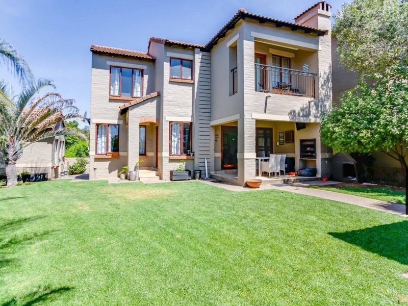 Rear view of a double-story house featuring a well-maintained lawn, a covered patio with a built-in braai, and an upper-level balcony.