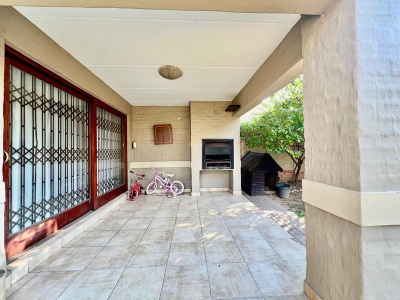 A covered patio area featuring tiled flooring and a built-in braai, providing a functional outdoor space for entertainment.