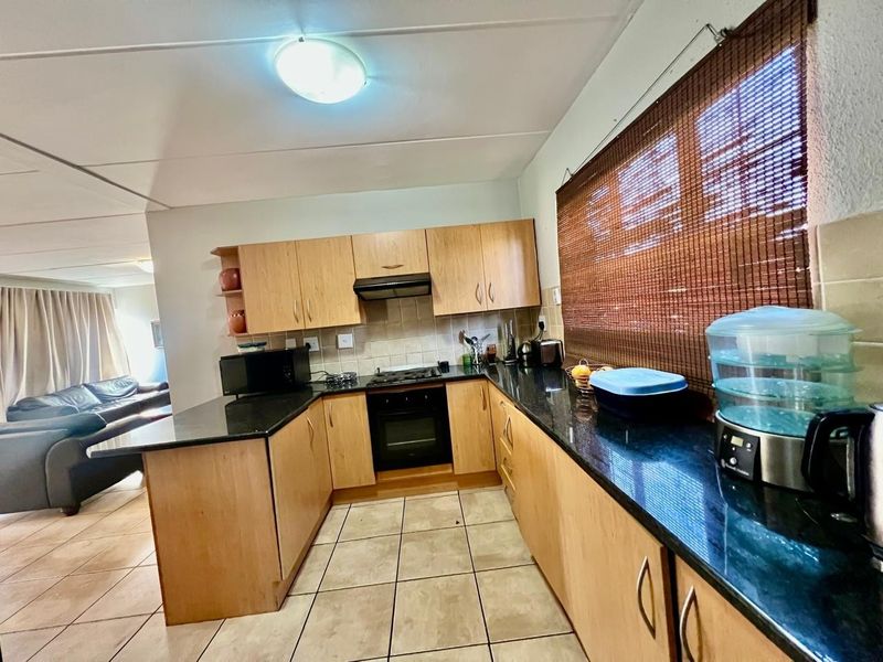 A functional kitchen featuring light wood cabinetry, dark granite countertops, built-in oven, gas hob, and tiled flooring, with an open-plan layout to the living area.