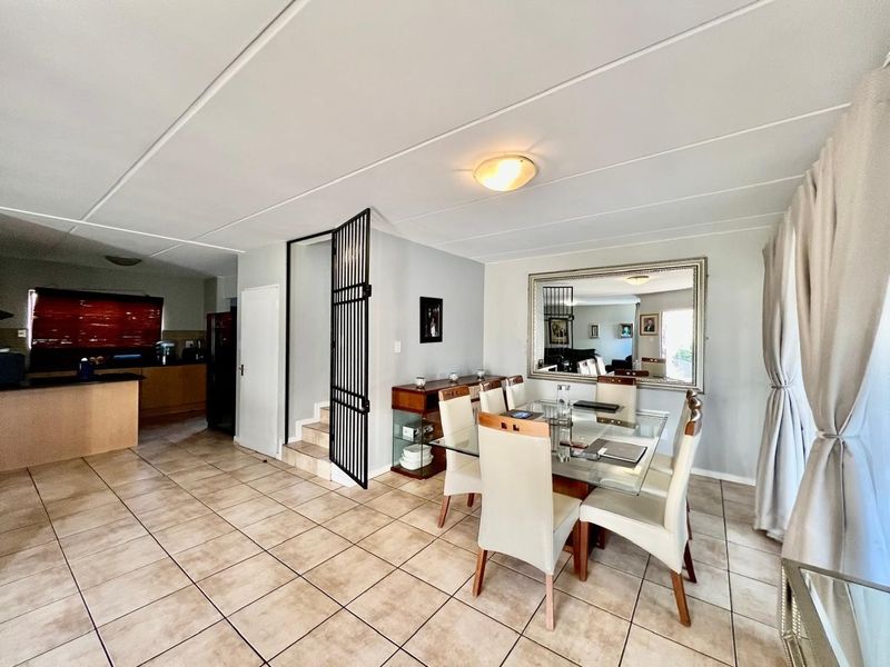 Open plan dining area featuring tiled flooring, a security gate leading to the staircase, and a view into the adjacent kitchen space.