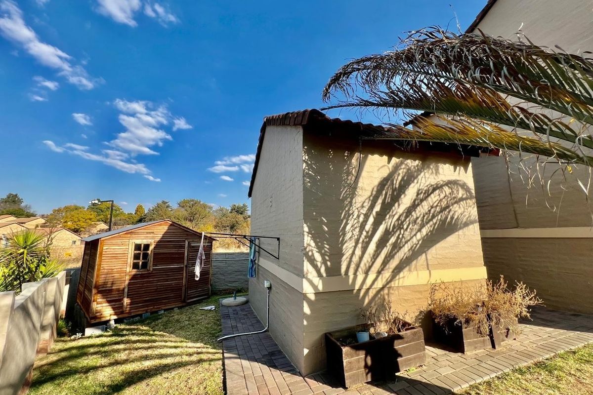 Rear exterior view of the property featuring a paved walkway, a wooden garden shed, and a wall-mounted clothesline against the main structure.