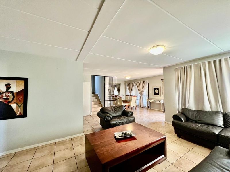 Spacious open-plan living and dining area featuring neutral tiled flooring, a security gate leading to the staircase, and ample natural light.