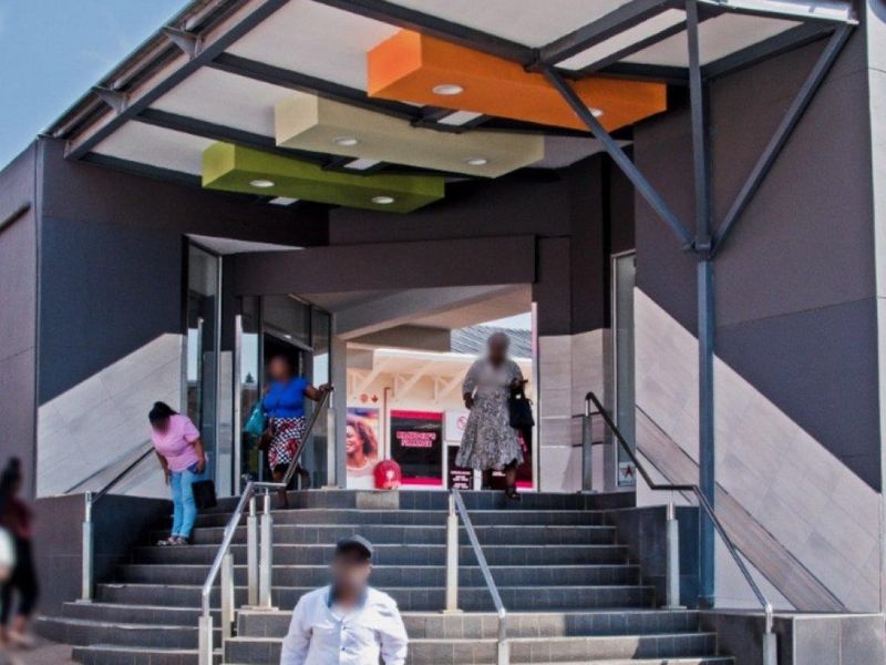 Modern commercial building entrance featuring a prominent steel canopy, decorative ceiling accents, and a wide concrete staircase with stainless steel handrails.