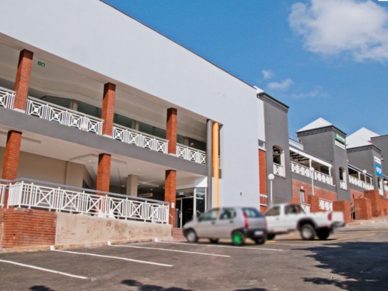 A multi-level commercial building facade featuring brick columns, white balustrades, and a paved parking area in front.