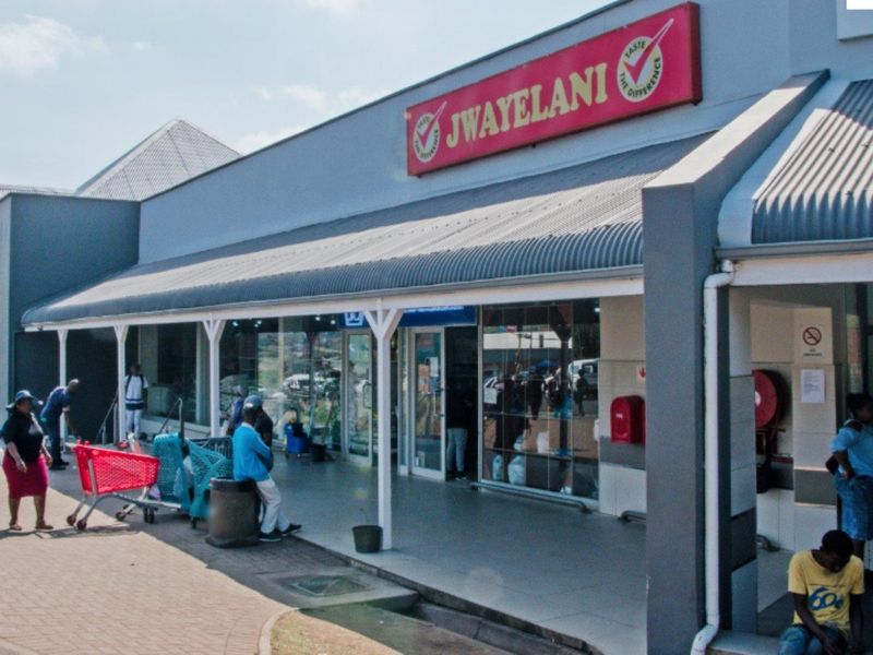 Front elevation of a commercial retail unit featuring a covered walkway, glass storefront, and prominent signage.
