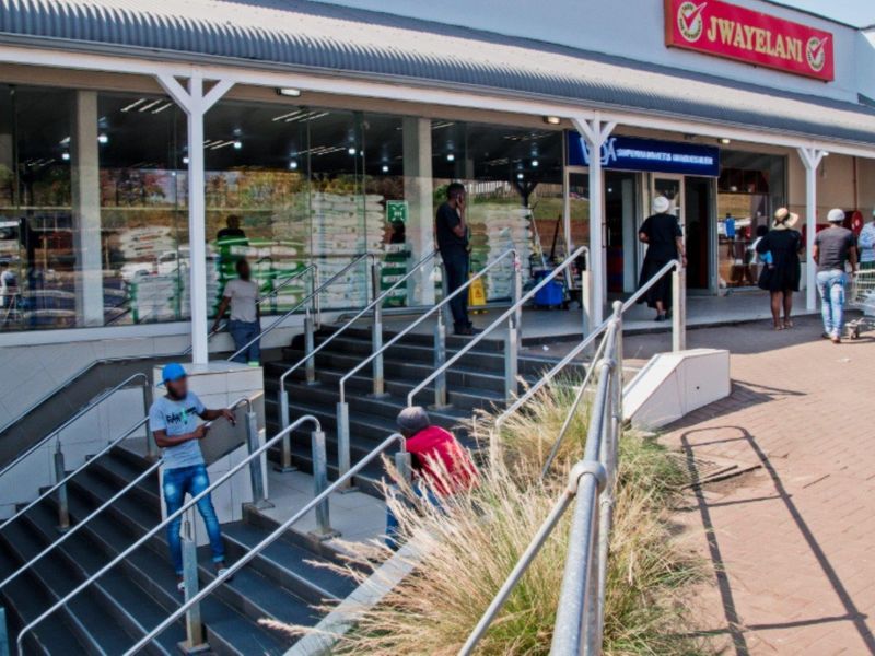 Front exterior view of a commercial retail building featuring a large glass storefront, metal staircase access, and a covered walkway.