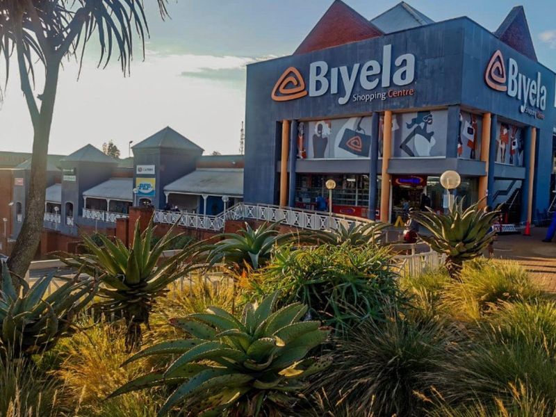 Exterior view of the Biyela Shopping Centre featuring a prominent facade, paved walkways, and landscaped garden areas.