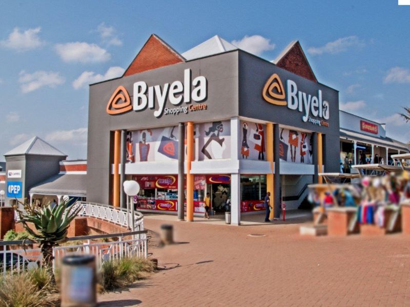 Exterior view of the Biyela Shopping Centre, featuring a modern commercial facade, paved pedestrian walkways, and prominent signage.