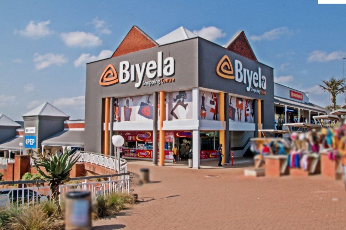 Exterior view of the Biyela Shopping Centre, featuring a modern commercial facade, paved pedestrian walkways, and prominent signage.