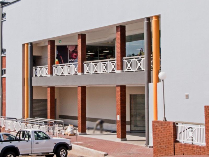 Front elevation of a commercial building featuring brick columns, metal railings, and ground-level roller shutter access points.