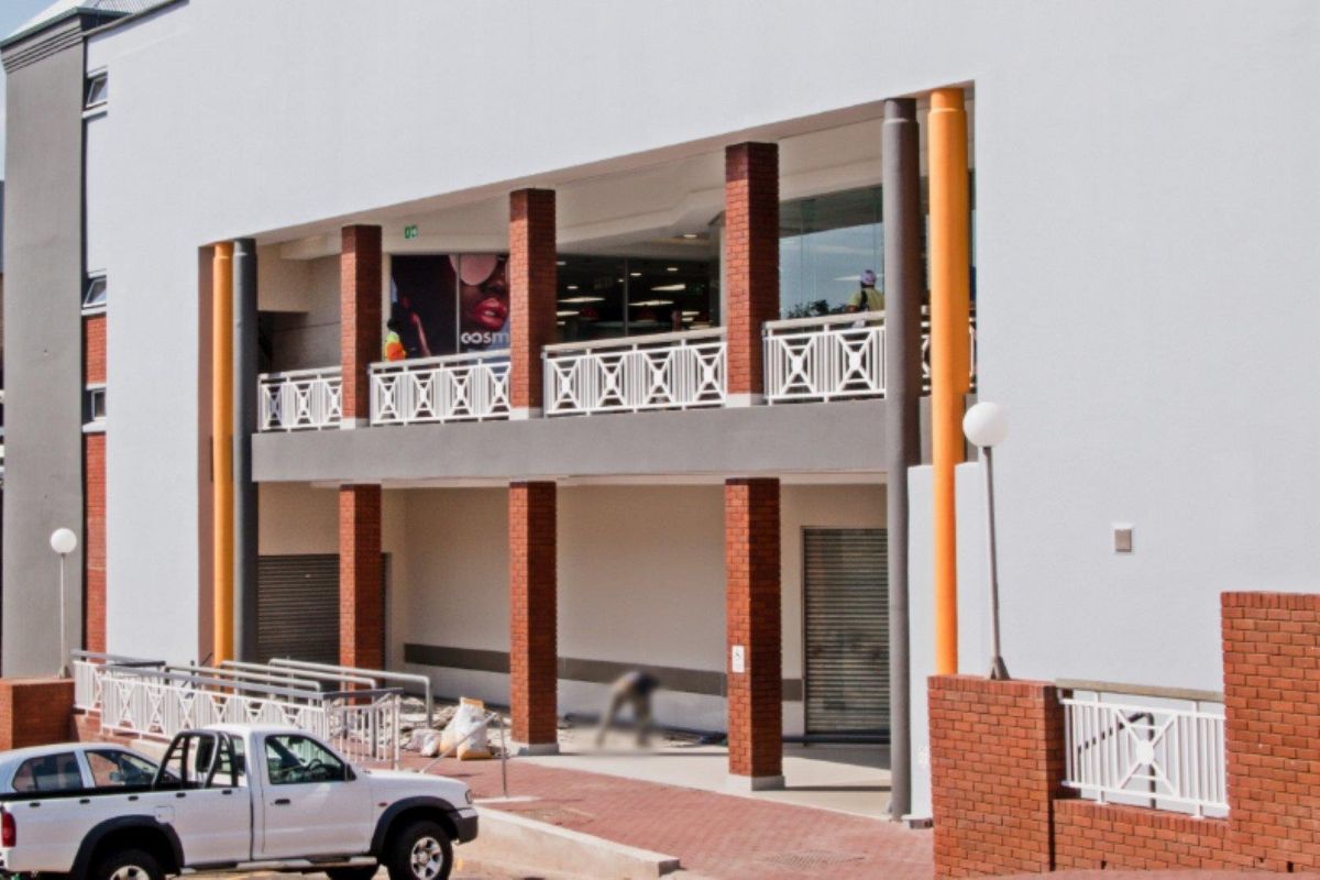 Front elevation of a commercial building featuring brick columns, metal railings, and ground-level roller shutter access points.