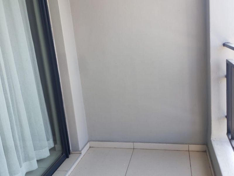 A clean, empty balcony featuring tiled flooring, a sliding glass door entrance, and a metal balustrade.