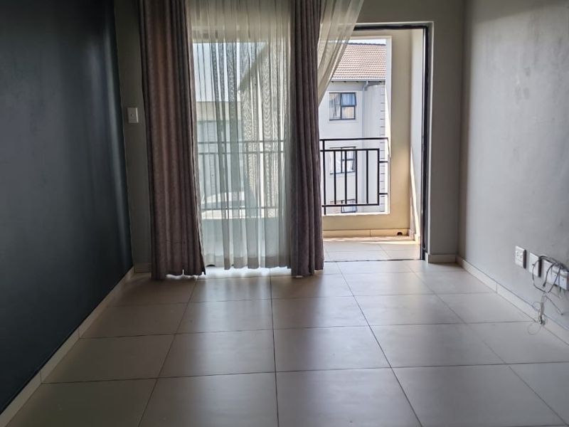 An empty living room featuring tiled flooring, a dark accent wall, and a sliding glass door providing access to a private balcony.