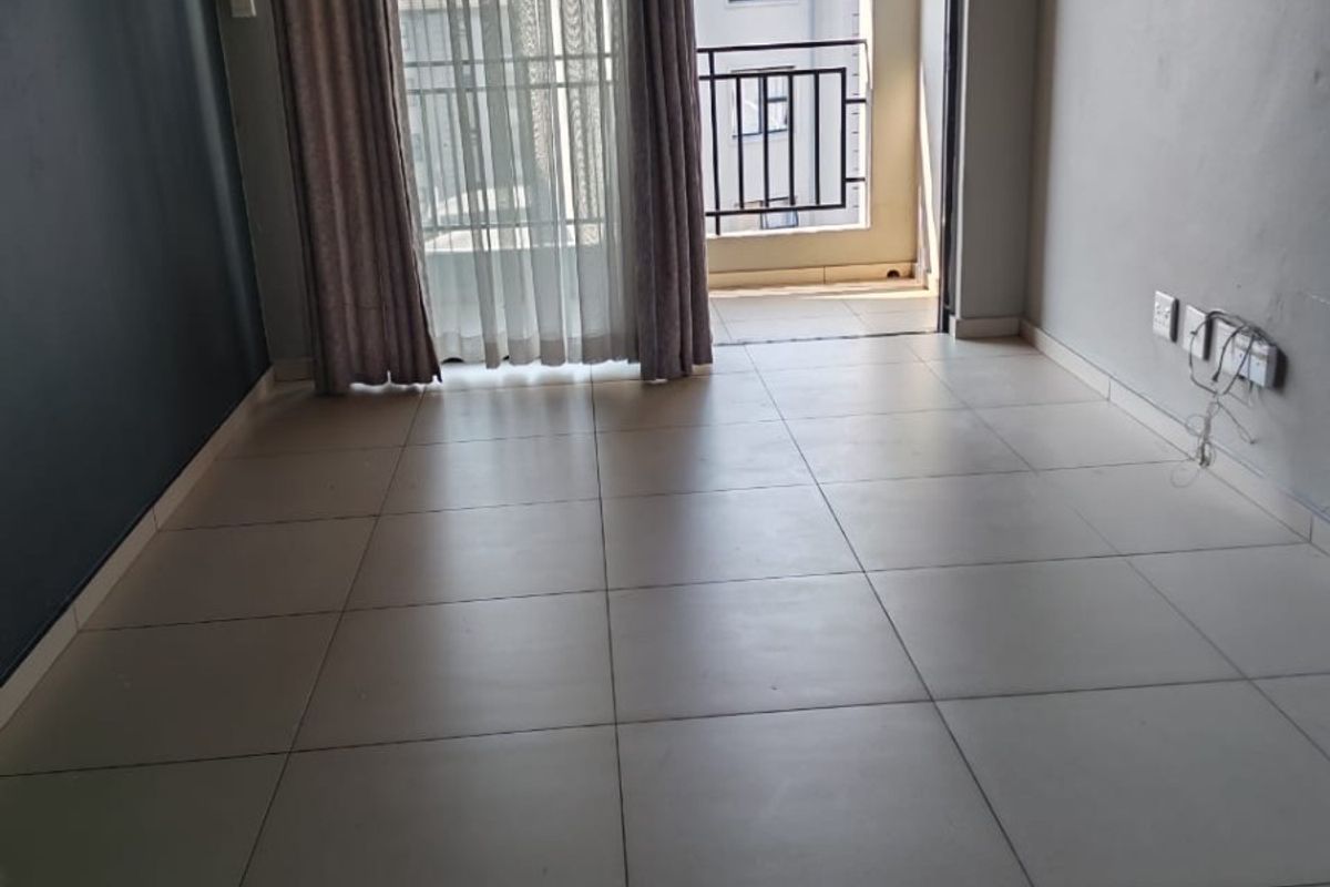 An empty living room featuring tiled flooring and a sliding glass door providing access to a private balcony.