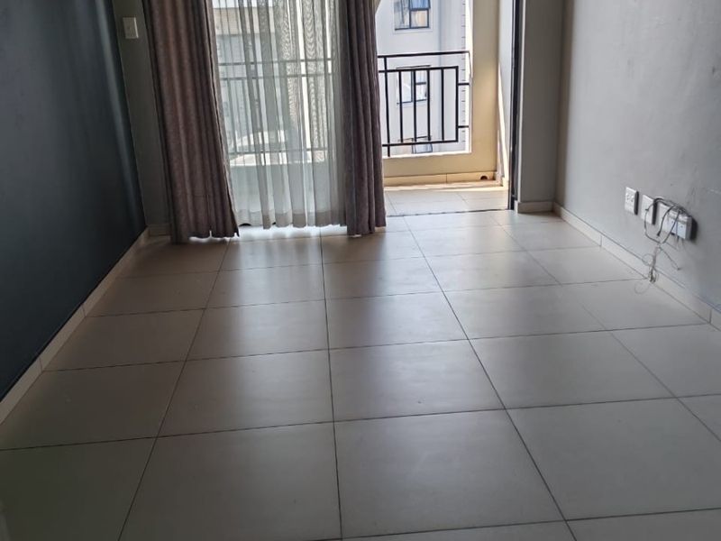 An empty living room featuring tiled flooring and a sliding glass door providing access to a private balcony.