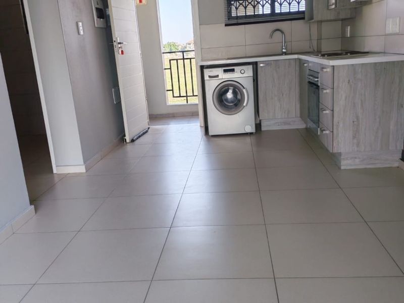 A clean, modern kitchen featuring light wood-finish cabinetry, tiled flooring, and integrated appliances, with direct access to an outdoor balcony area.