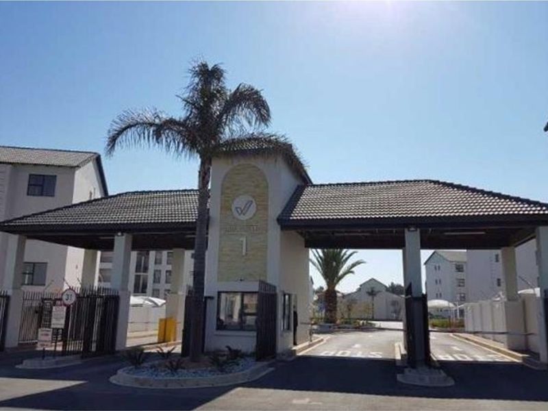 A secure gated entrance to the apartment complex featuring a manned security gatehouse, access control infrastructure, and paved driveway.